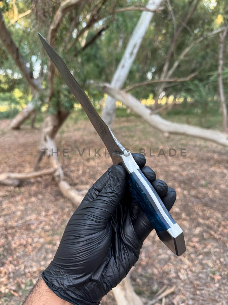 Hand holding a knife with 'The Viking Blade' branding against a natural background.