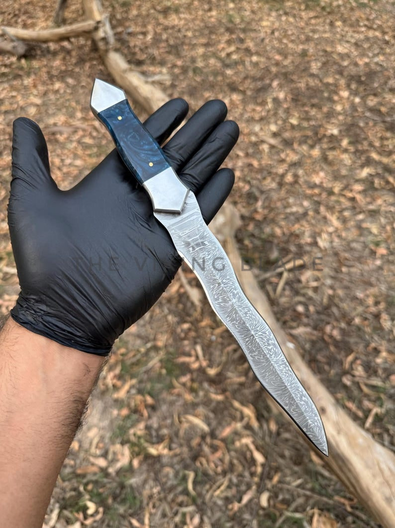 Knife with a black handle held by a gloved hand against a natural background