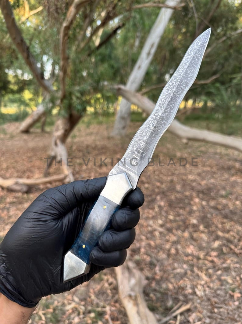 Knife held by a gloved hand with a natural outdoor background