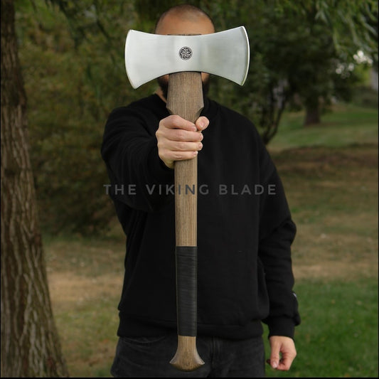 Person holding a large axe in front of their face outdoors