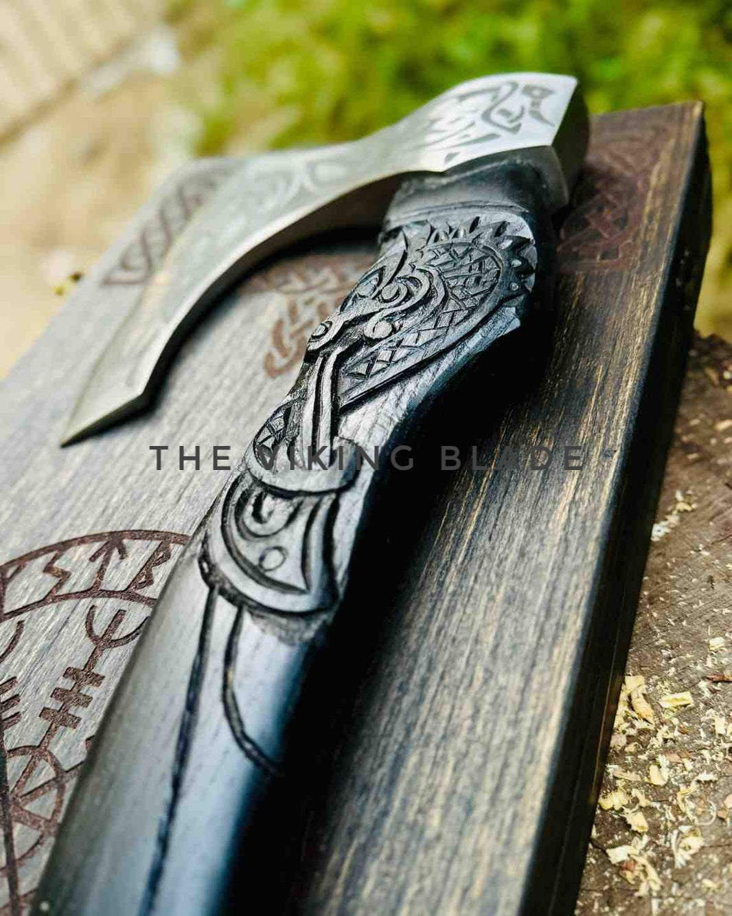 Decorative Viking-style axe with intricate designs on a wooden stand, featuring the brand 'The Viking Blade'.