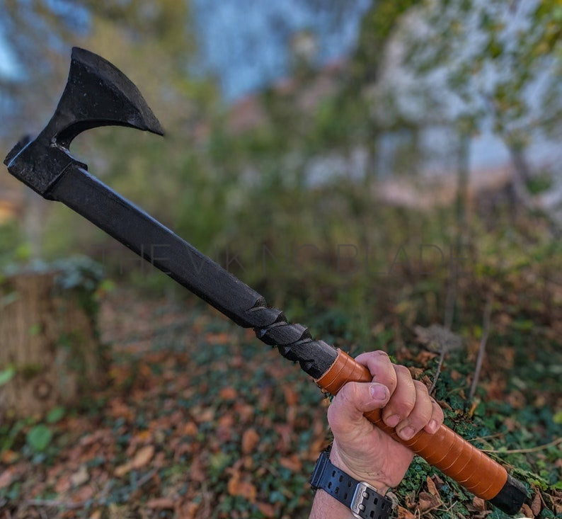 Person holding a black axe with a braided wooden handle in a forest setting