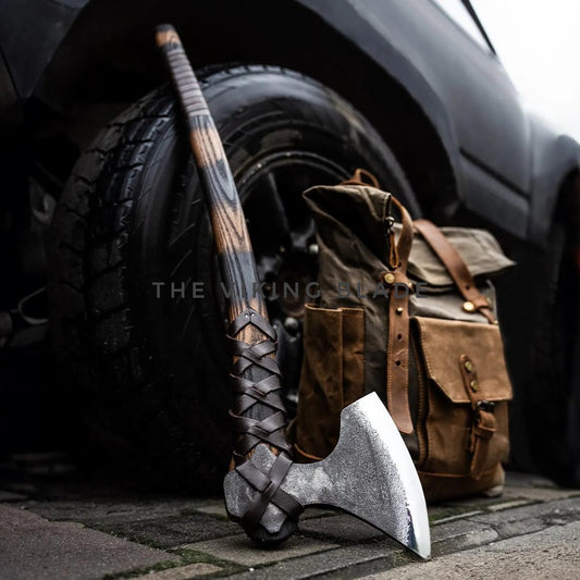 Ax leaning against a car tire with a leather bag in the background