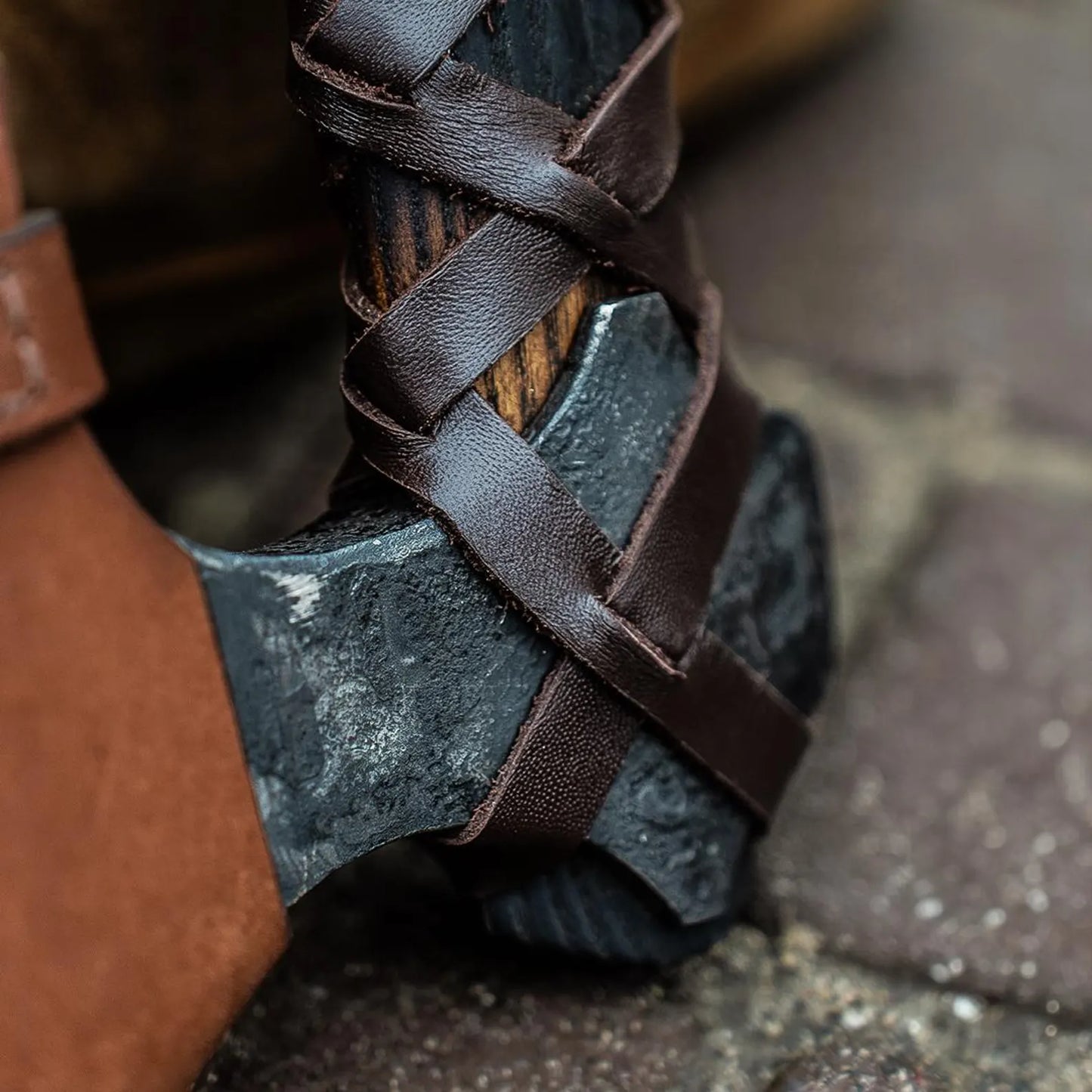 Close-up of a black axe with leather straps on a stone surface