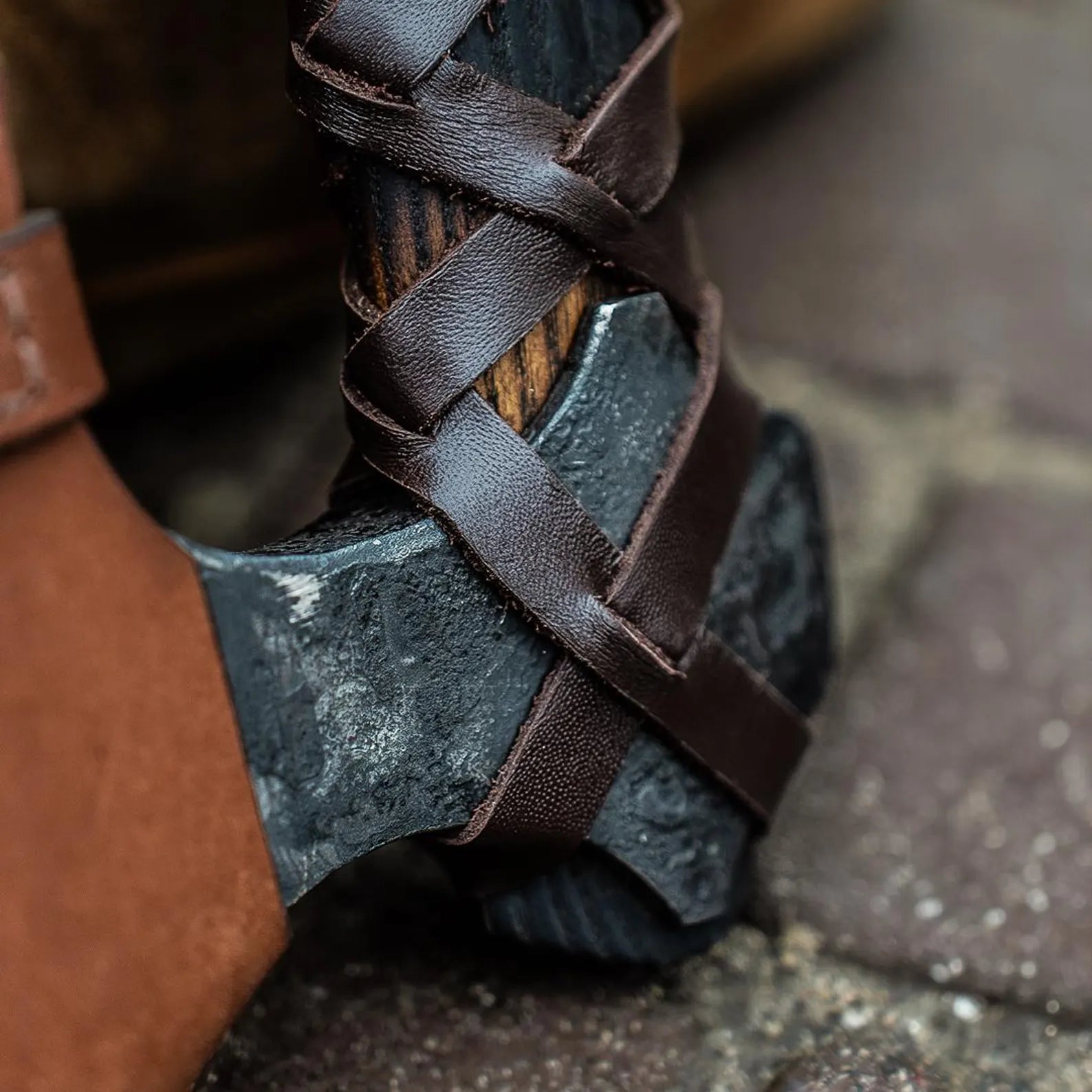 Close-up of a black axe with leather straps on a stone surface