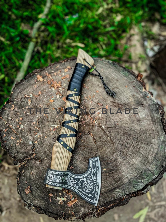 Decorative axe with wooden handle and black blade on a tree stump, branded 'The Viking Blade'.