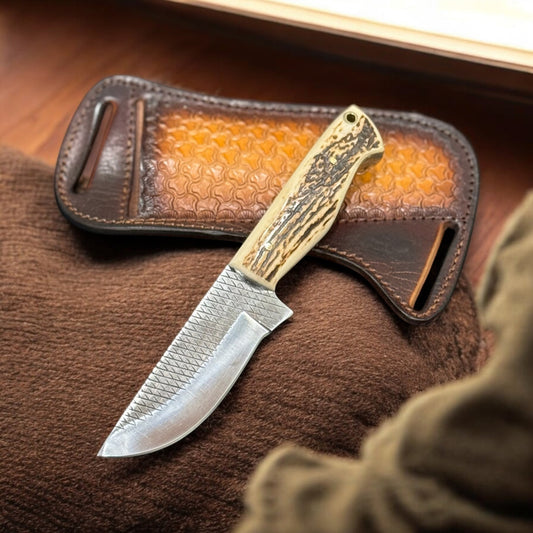 A knife with a stag horn handle and a leather belt sheath in the background.