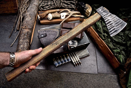 Hand holding a wooden-handled axe over a rustic setting with tools and leather goods.