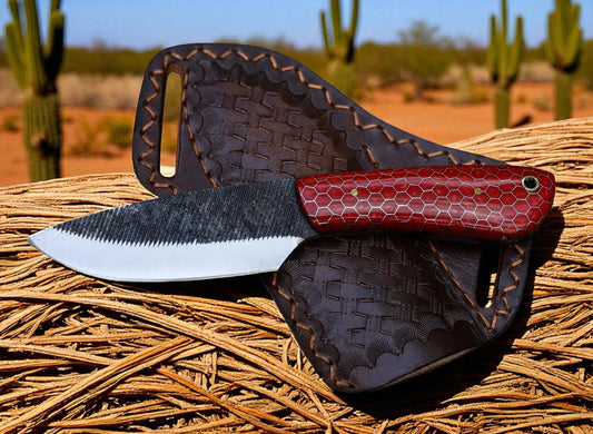 Knife with red handle and black blade in a leather sheath against a desert background with cacti.