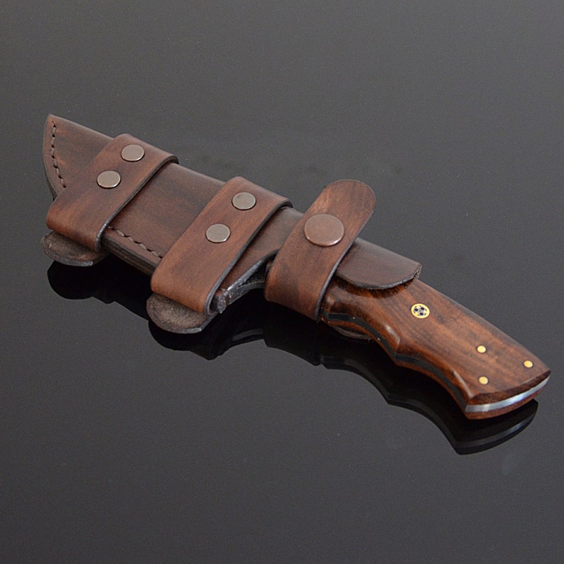 Knife with wooden handle and brown leather sheath on a dark background