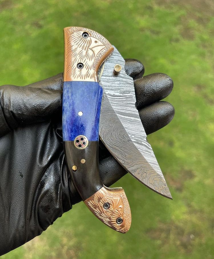 Folding knife with decorative handle and blade held by a gloved hand against a green background