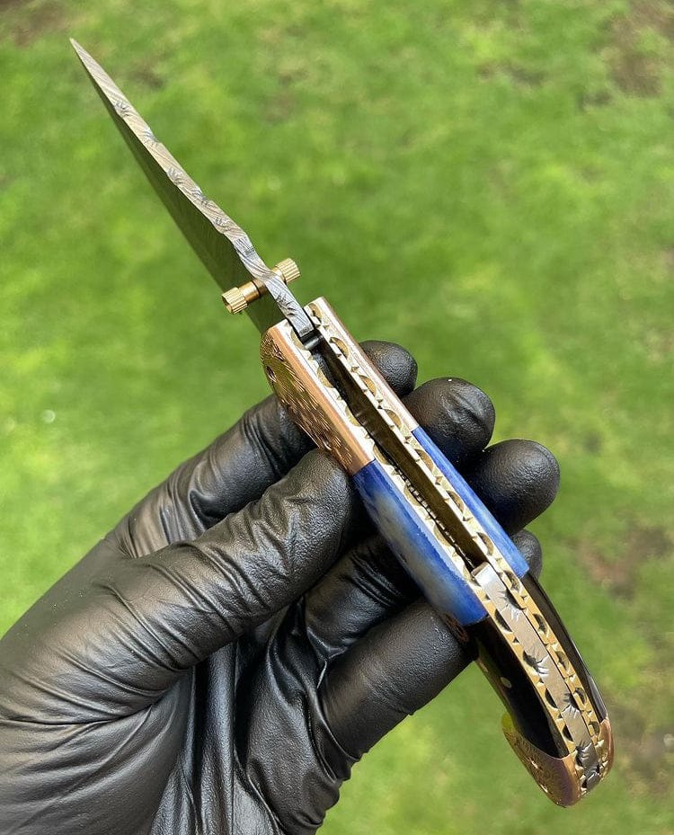 Knife with a metallic blade and wooden handle held by a gloved hand against a green outdoor background
