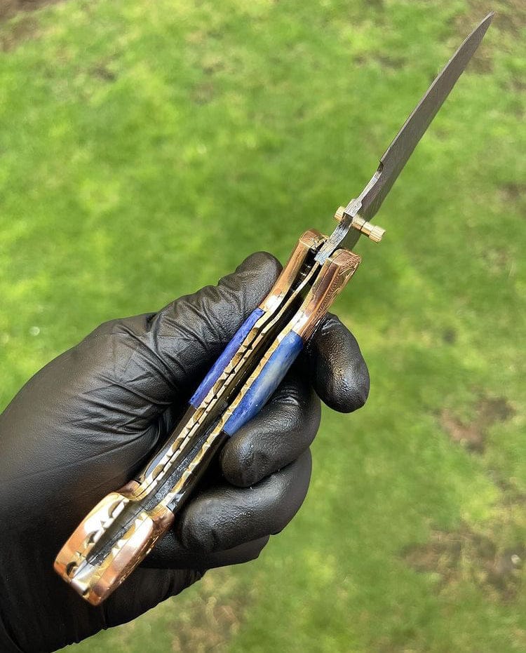 Hand holding a folding knife with a green grass background