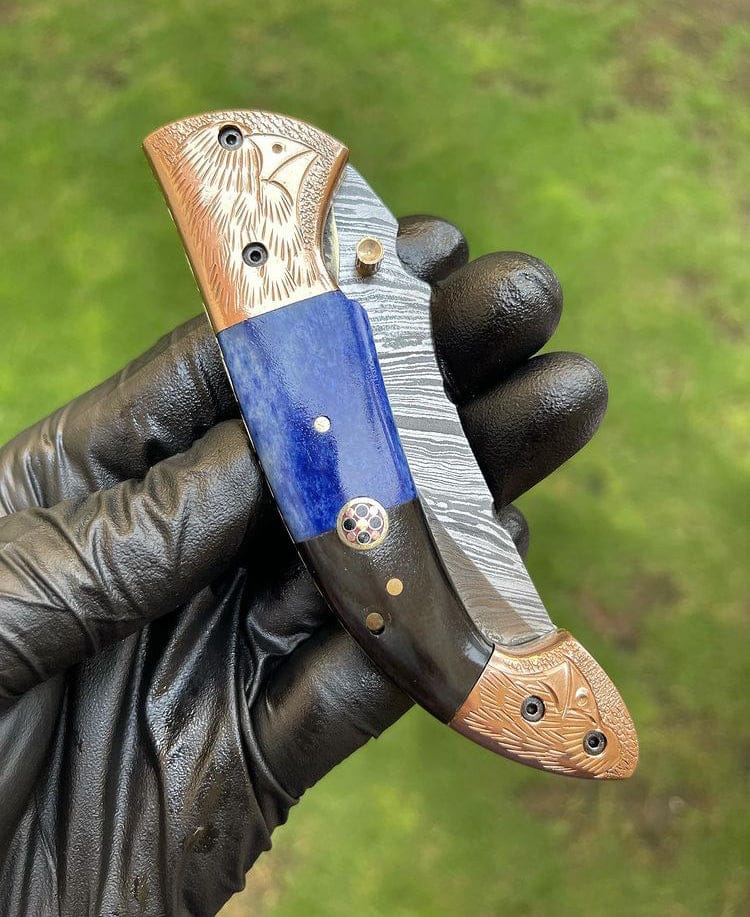 Folding knife with decorative handle held by a gloved hand against a green background