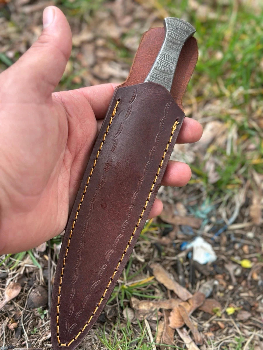 Hand holding a knife with a leather sheath against a natural background