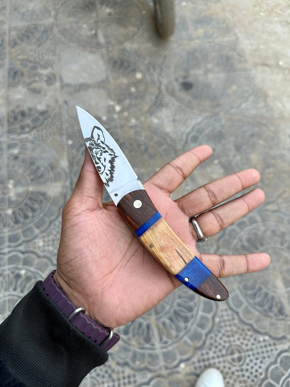 Hand holding a knife with a wooden handle and metal blade on a textured pavement background