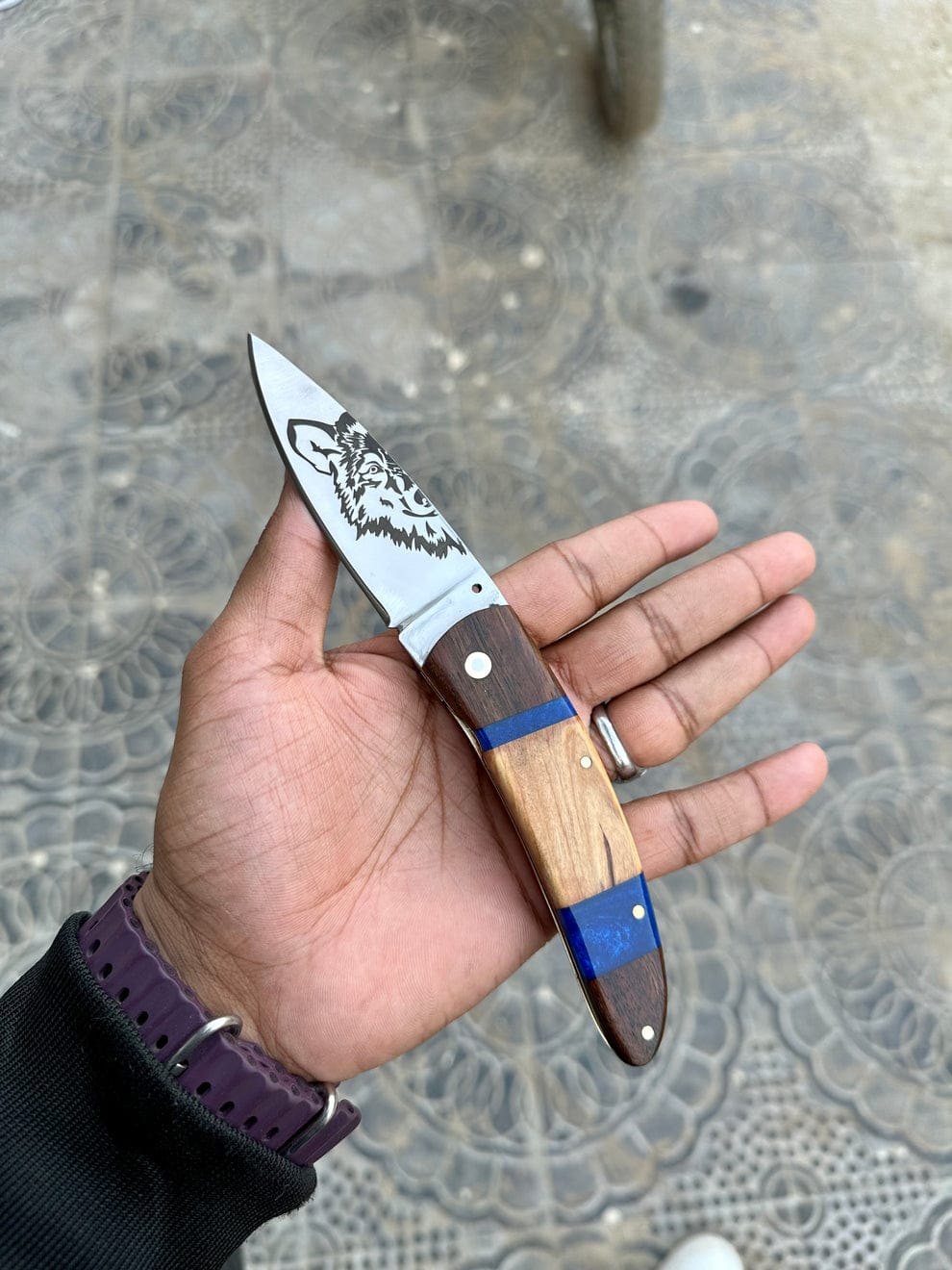Hand holding a pocket knife with a wooden handle and metal blade on a textured surface.