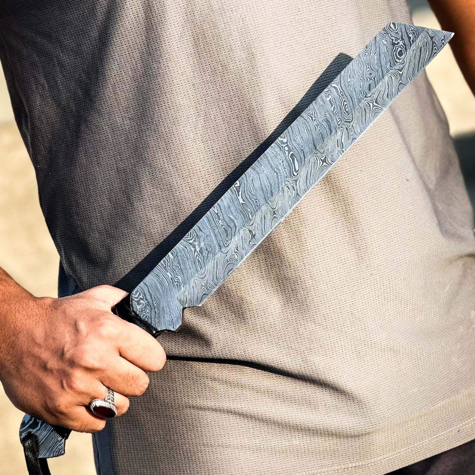 Person holding a large Damascus steel knife against a neutral background