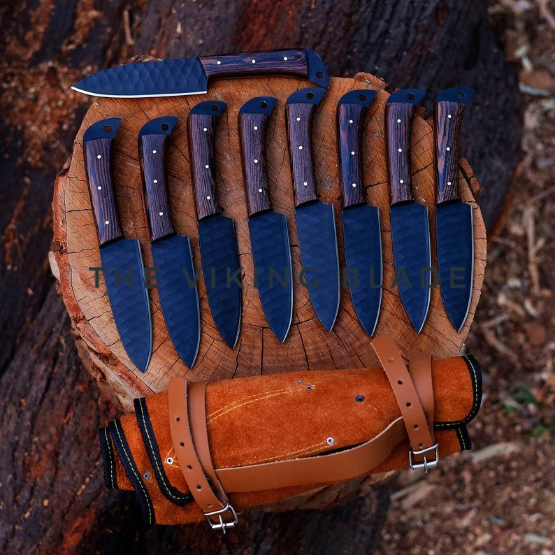 A set of handmade steak knives with black and brown leather roll, displayed on a wooden surface.