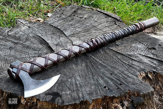 A Nordic axe with a leather-wrapped handle, high carbon steel head, and a decorative leather cover lying on a wooden stump.