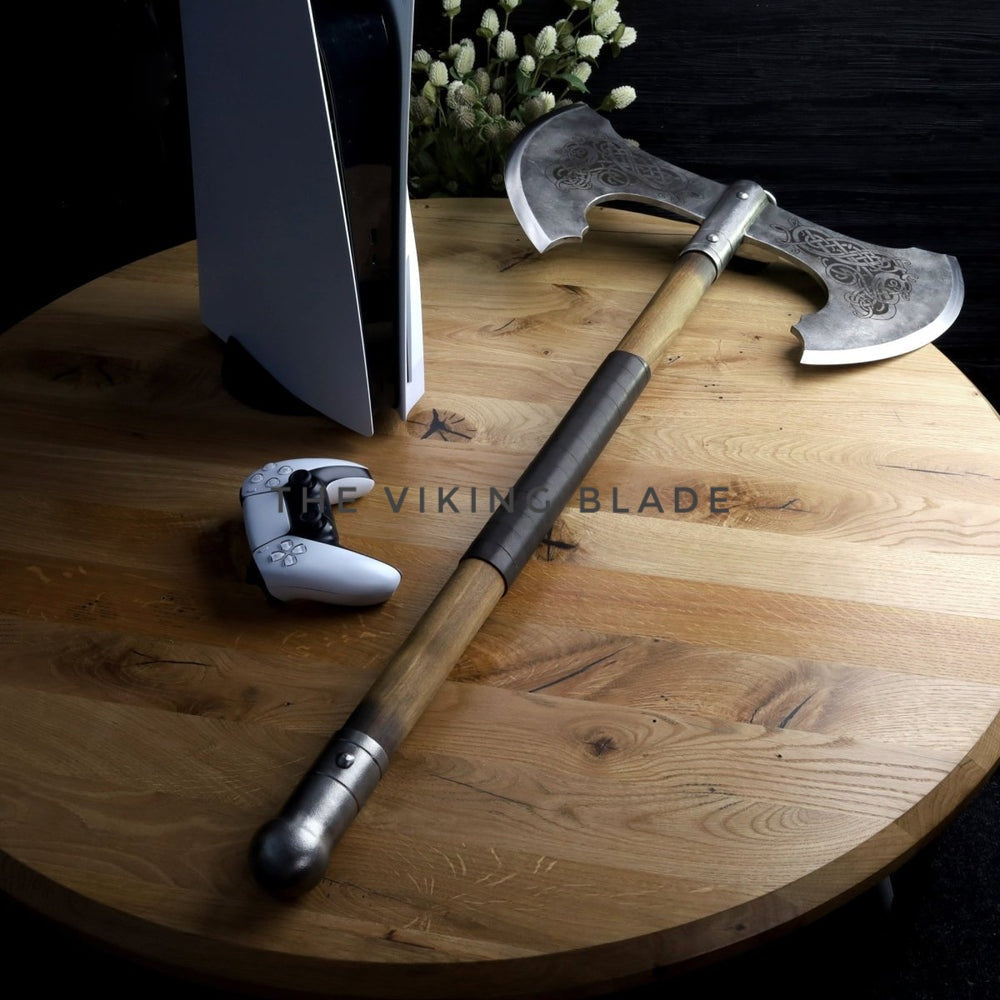 Decorative axe with wooden handle and metal head on a wooden surface next to a gaming console and controller.