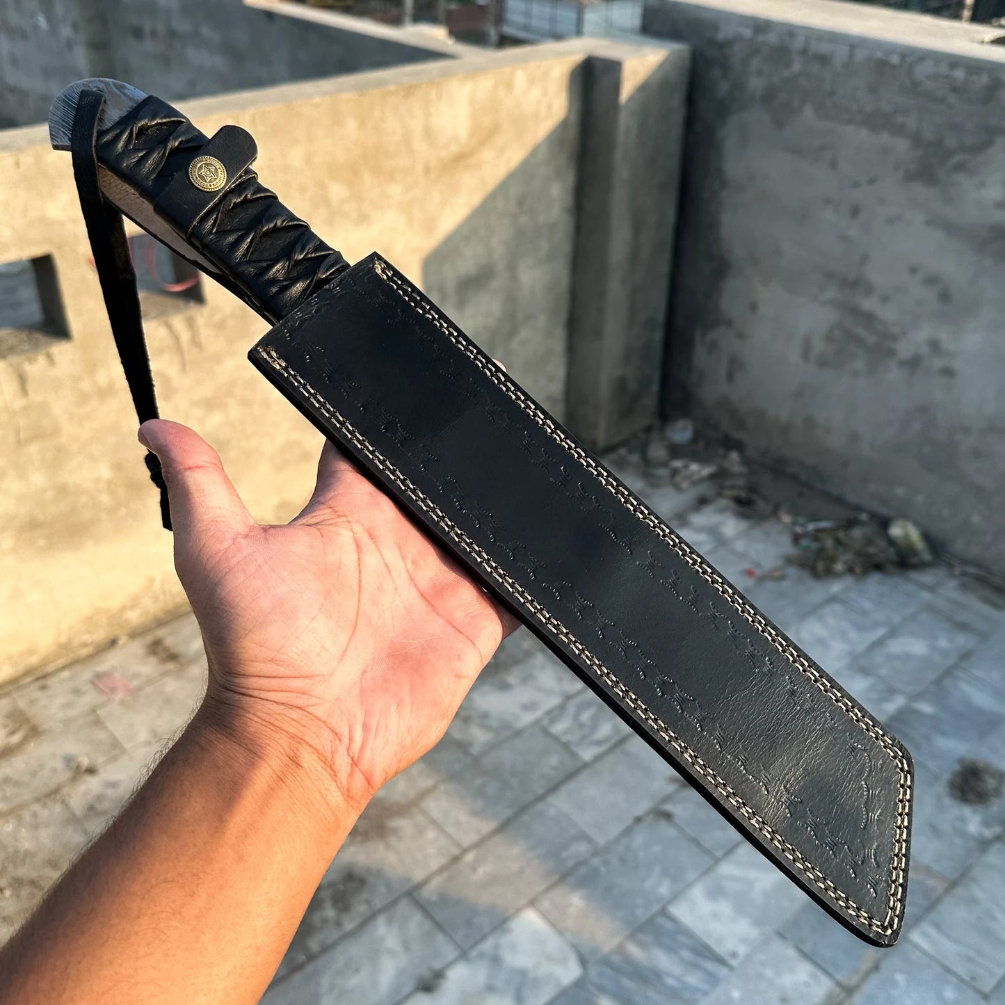 Hand holding a black leather knife sheath against a concrete wall background
