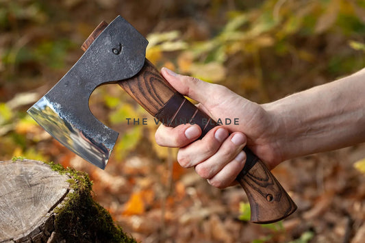 Hand holding a axe with 'The Viking Blade' branding against a blurred natural background