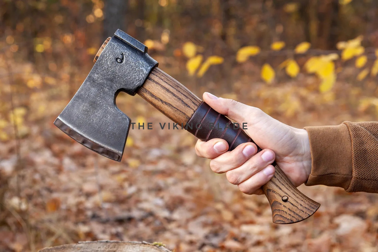 Hand holding a axe with a wooden handle against an autumn forest background