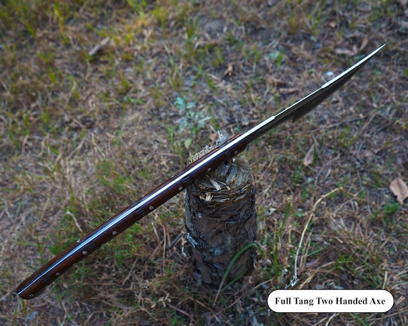 Full tang two handed axe on a tree stump with grass in the background
