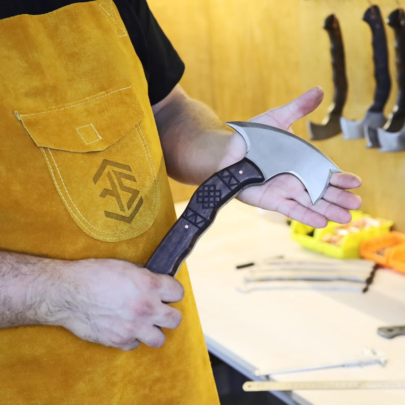 Person holding a large axe with a yellow apron featuring a logo.