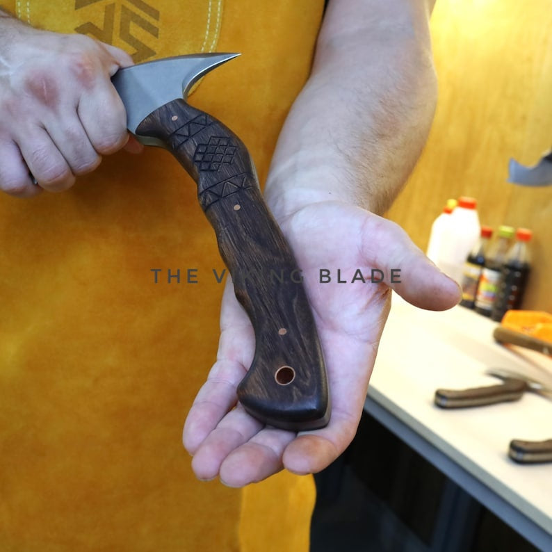 Hand holding a wooden-handled knife with 'The Viking Blade' branding against a blurred background.
