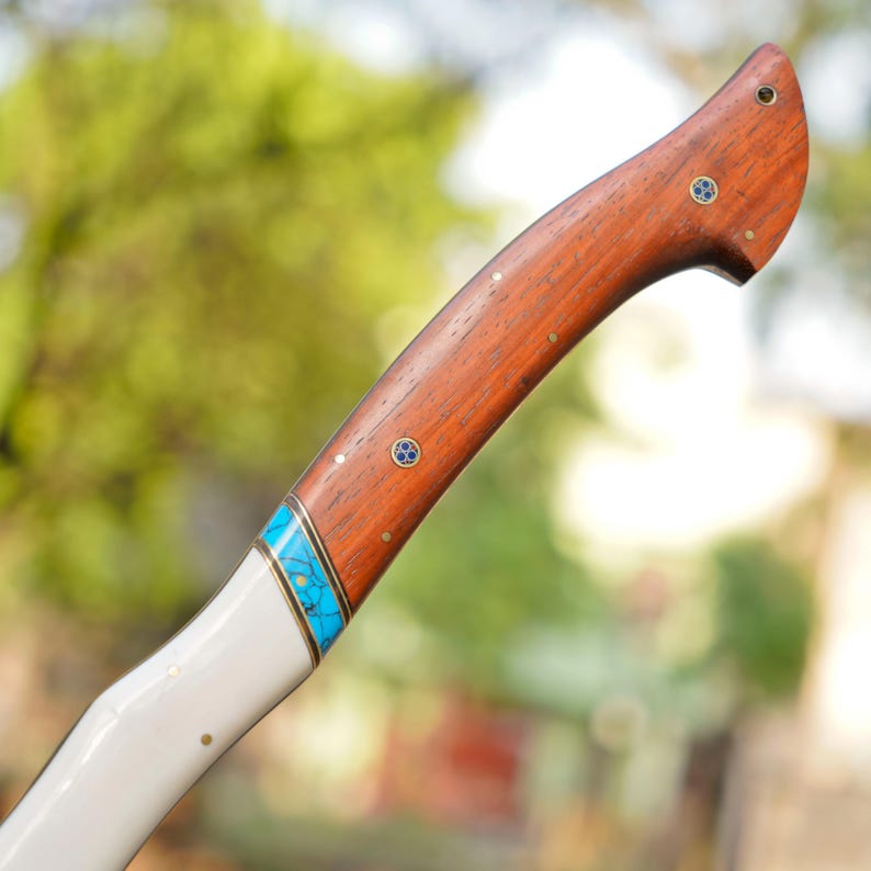 Wooden-handled tool with white shaft and blue inlay against a blurred natural background