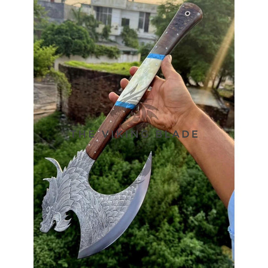 Hand holding a decorative axe with a detailed blade against a natural background