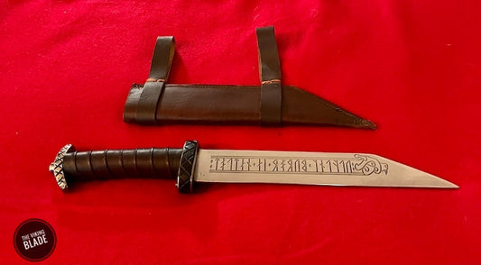 A Viking seax with a leather wrapped handle and a blade engraved with runes, accompanied by a red leather sheath, displayed on a red background.