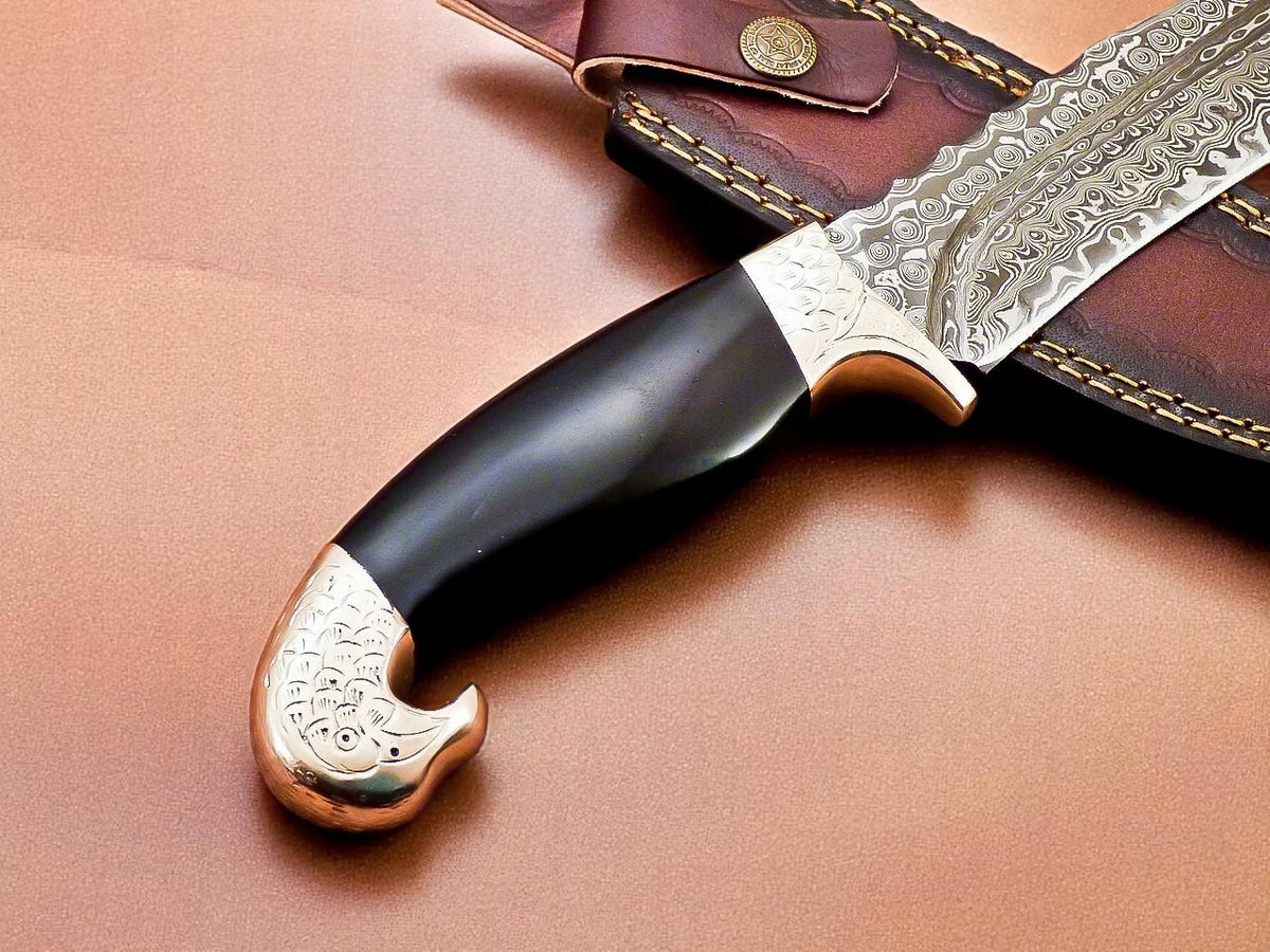 Decorative knife with black handle and gold embellishments on brown leather background.