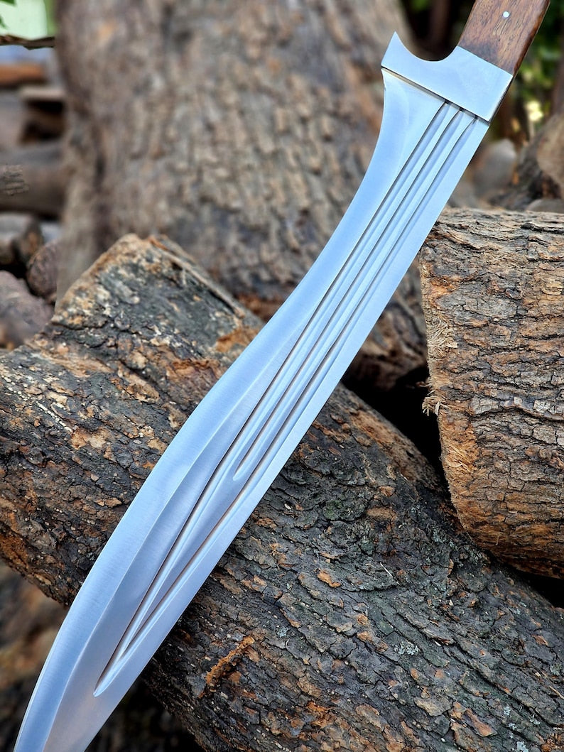 A curved silver steel knife with a wooden handle, resting diagonally on rough tree logs outdoors.