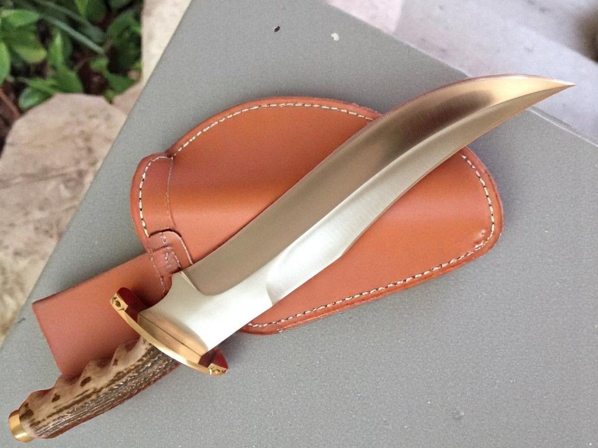 A custom handmade hunting Bowie knife with a brown leather sheath, featuring a stag handle with brass clip and pommel.