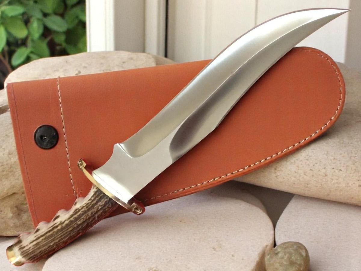 Knife with antler handle in leather sheath on stone surface.