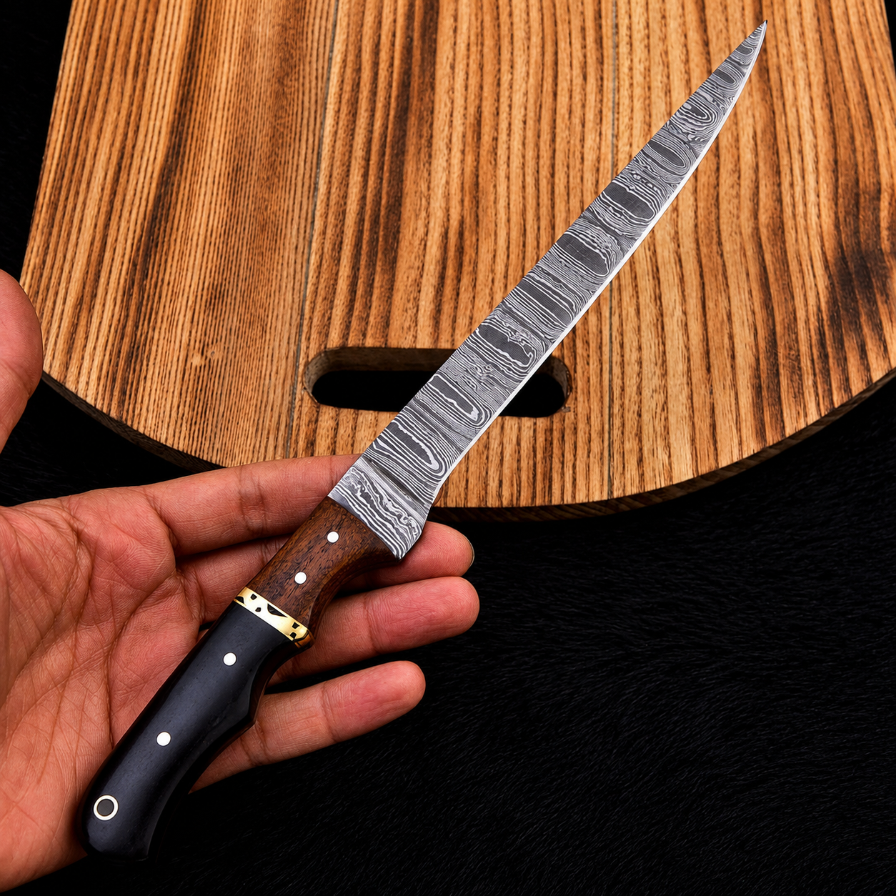 A hand holding a long Damascus steel knife with a patterned silver blade, brown wooden handle, and black bolster, positioned diagonally over a wooden cutting board.