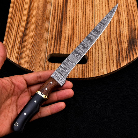 A hand holding a long Damascus steel knife with a patterned silver blade, brown wooden handle, and black bolster, positioned diagonally over a wooden cutting board.