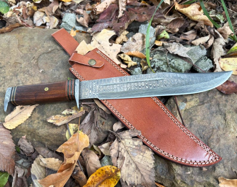 Knife with wooden handle and leather sheath on leafy background