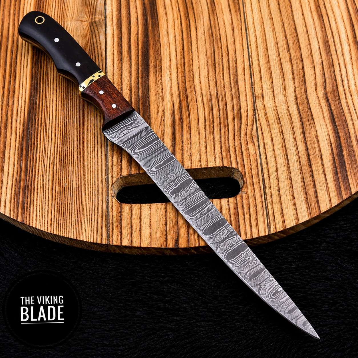 A custom Damascus steel knife with a wavy patterned blade, a dark brown wood handle, and brass bolsters, resting diagonally on a wooden cutting board. A black textured background is visible at the bottom, with a circular logo in the lower-left corner reading 'THE VIKING BLADE'.