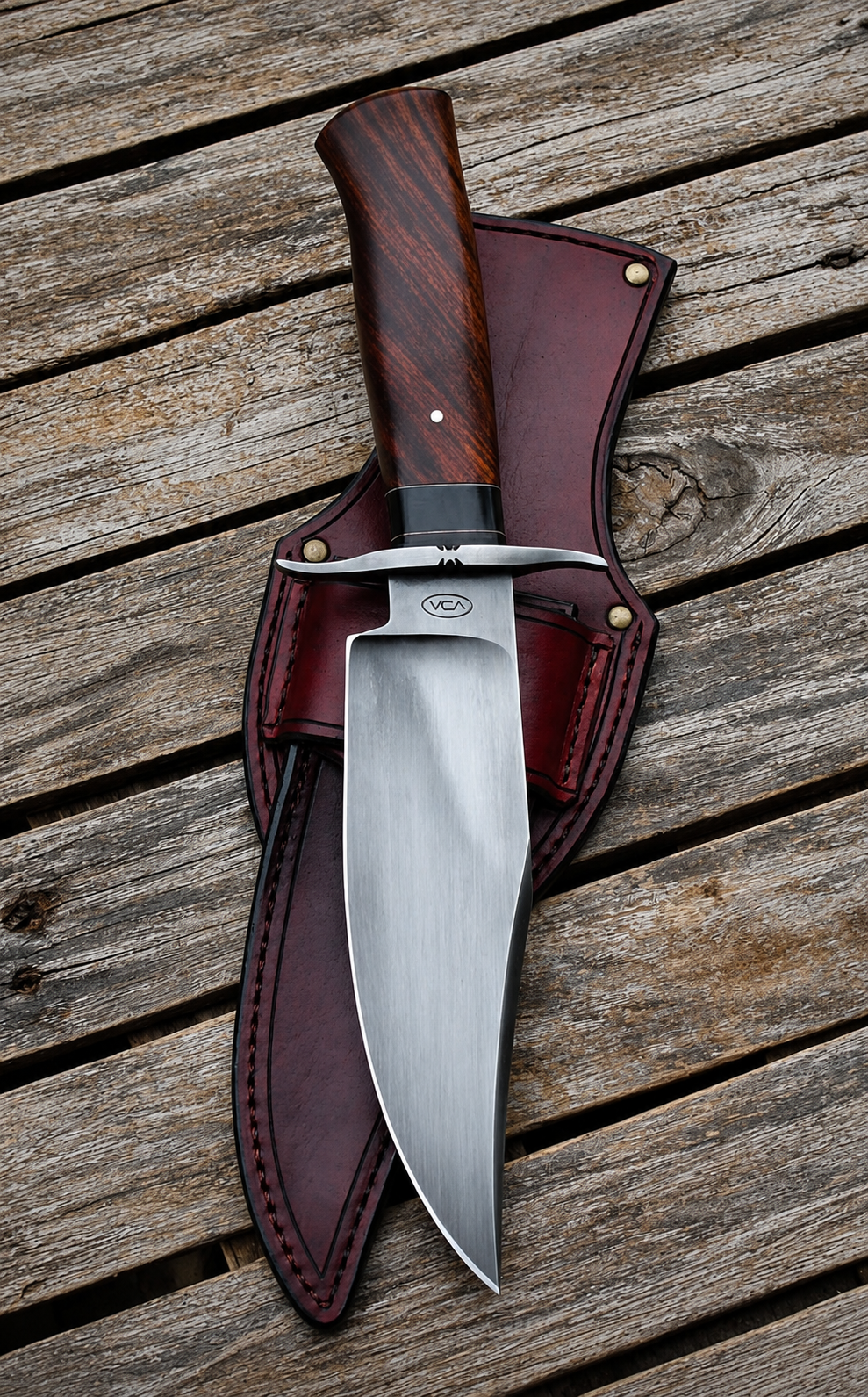 A fixed-blade knife with a polished silver blade and a dark wood handle, resting diagonally on a dark brown leather sheath over a weathered wooden plank surface.