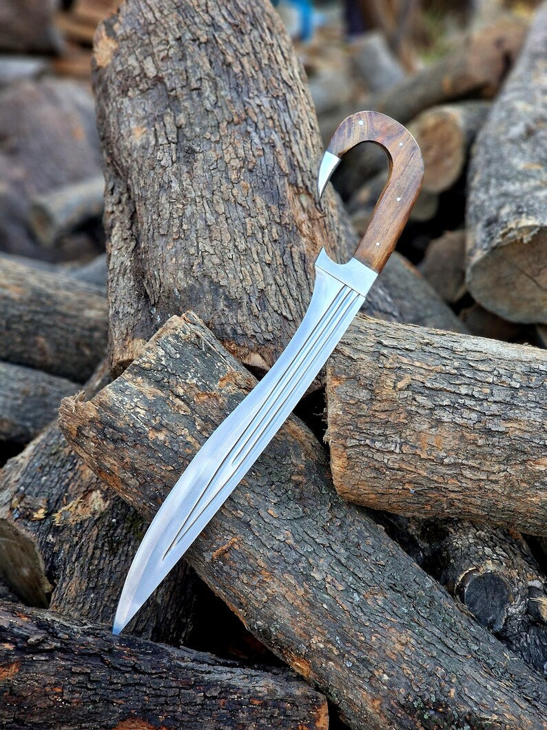 A curved fixed-blade knife with a silver blade and a brown wooden handle, resting on a pile of cut logs and bark.