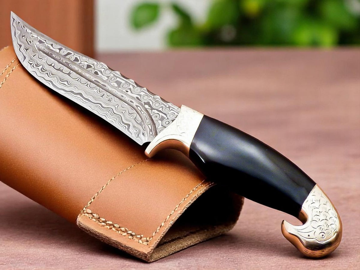Decorative knife with black handle and silver blade on a brown leather sheath.