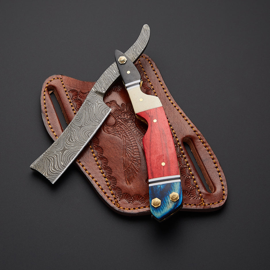 A folding pocket knife with a Damascus steel blade, a red and blue wood handle, and brass hardware, displayed diagonally over its brown tooled leather sheath on a dark gray background.