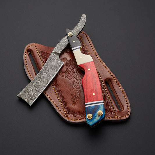 A folding pocket knife with a Damascus steel blade, a red and blue wood handle, and brass hardware, displayed diagonally over its brown tooled leather sheath on a dark gray background.