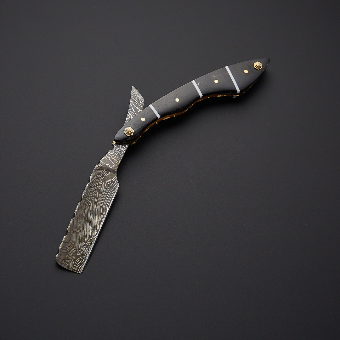 Damascus steel straight razor blade showing detailed wave pattern and precision-sharpened cutting edge.