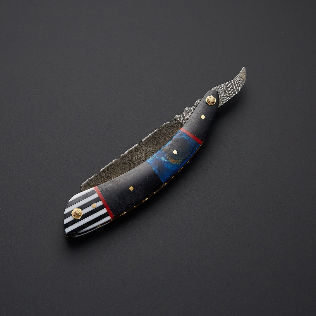 Artisan Damascus steel straight razor blade close-up showing detailed pattern forging and razor-sharp precision edge.