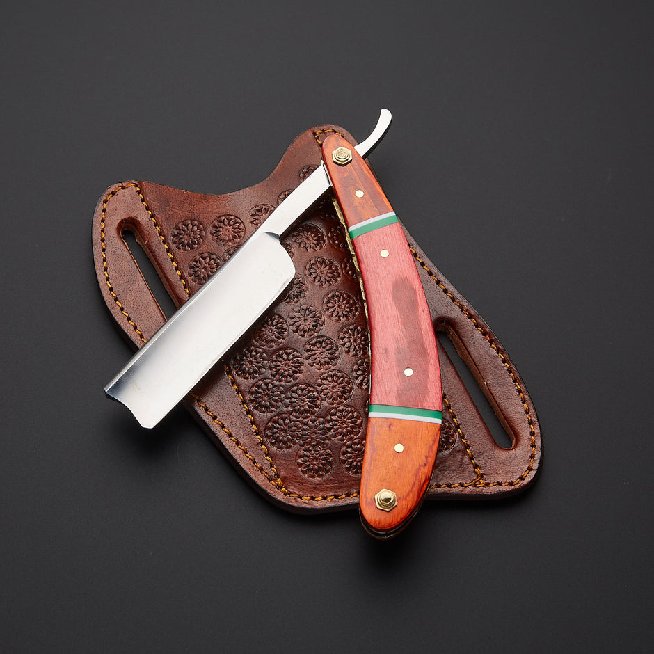 A straight razor with a reddish-brown wooden handle and green accents, displayed next to its embossed brown leather sheath on a dark background.